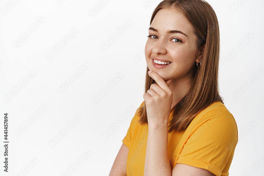 Beauty and people concept. Close up portrait of attractive young woman smiling pleased, touch chin and look thoughtful at camera, standing confident against white background Beauty and people concept. Close up portrait of attractive young woman smiling pleased, touch chin and look thoughtful at camera, standing confident against white background