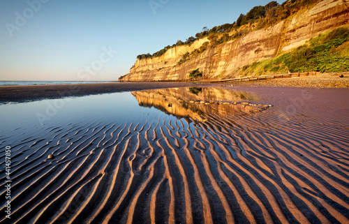 Shanklin beach on the isle of wight, with ripples in the sand and reflection of cliffs in the pool of water.