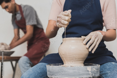 partial view of young african american woman squeezing sponge while shaping wet clay pot on wheel near blurred man in pottery