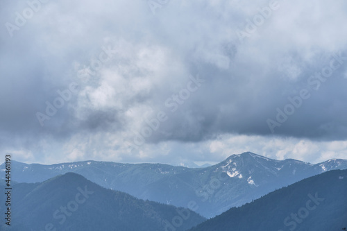 Silhouettes of snow capped mountains in distance on horizon. Beautiful panorama of several Caucasian mountains located on ridge. Low clouds, weather before storm in mountains.