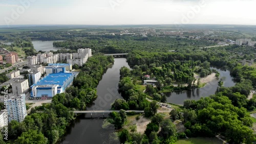 Panoramic drone view of a green city in northern Europe. Drone shot on an island with sandy beaches. Pedestrian bridge over the Psel river in Ukraine, the city of Sumy.People are relaxing on the beach photo