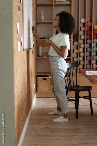 Focused young millennial african american woman in a casual clothes writes on the flip chart in the office