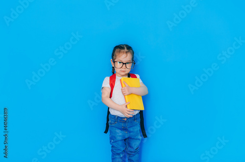 Back to school concept. School girl with red backpack and holding yellow folder in front of blue background