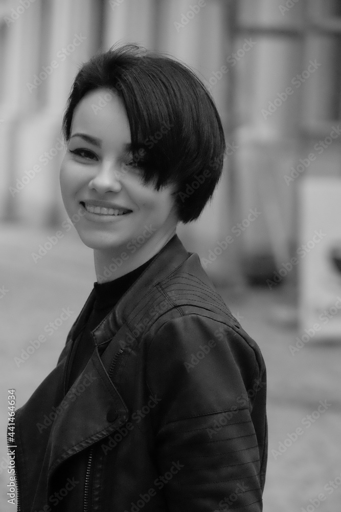 A happy young girl in a black leather jacket and short hair is sitting at a table. Black and white portrait of a smiling woman A happy young girl in a black leather jacket and short hair is sitting at a table. Black and white portrait of a smiling woman