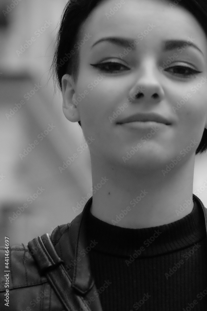 A happy young girl in a black leather jacket and short hair is sitting at a table. Black and white portrait of a smiling woman A happy young girl in a black leather jacket and short hair is sitting at a table. Black and white portrait of a smiling woman