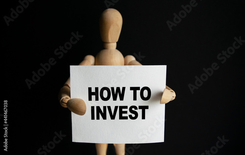 Wallpaper Mural The wooden man holds a white sign with the text HOW TO INVEST in his hands. The content of the lettering has implications for business concept and marketing. Torontodigital.ca