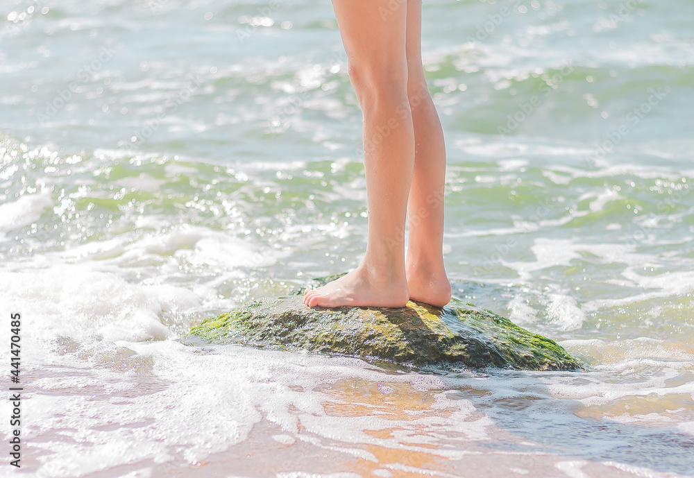 legs of a young girl stand on a stone in the water near the seashore. summer vacation concept legs of a young girl stand on a stone in the water near the seashore. summer vacation concept