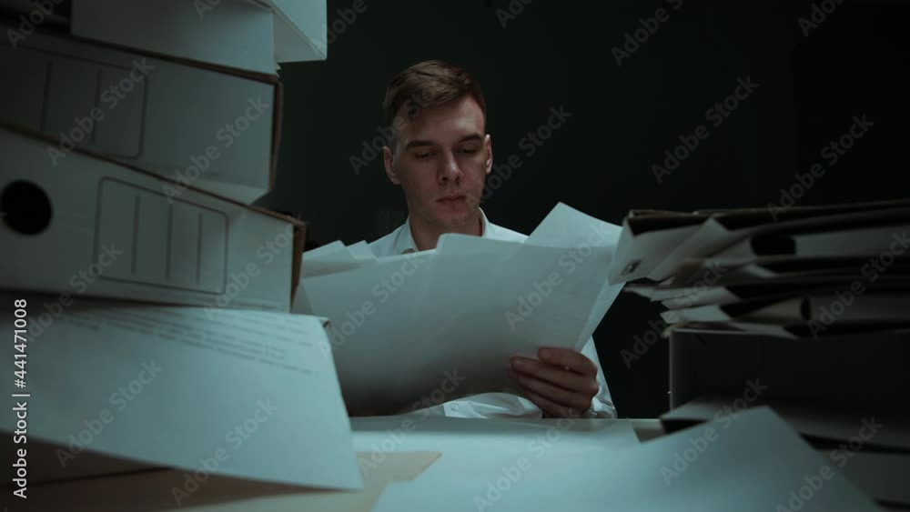 Tired man with pile of folders working in office, employee works with documents in evening having headache, getting new task, exhausted worker holding his head. Bad mood, fatigue, lots of work.