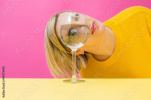Fashion woman portrait, eye looks through the glass of water. Object distortion, optical illusion. Minimalistic contemporary art.Beautiful woman's face in wine glass.Visual concept. photo