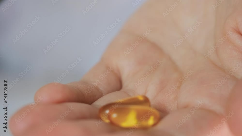 Close up hand female doctor lays out put yellow pills in hand. Tablets Omega 3 drugs being spill out from green plastic bottle. Close up hand female doctor lays out put yellow pills in hand. Tablets Omega 3 drugs being spill out from green plastic bottle.
