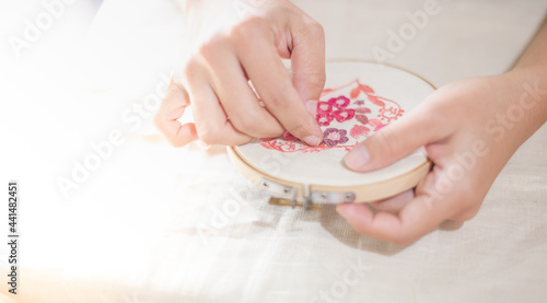Female hand holding wood embroidery frame and needle working on flower pattern stitching in a process of handiwork. photo