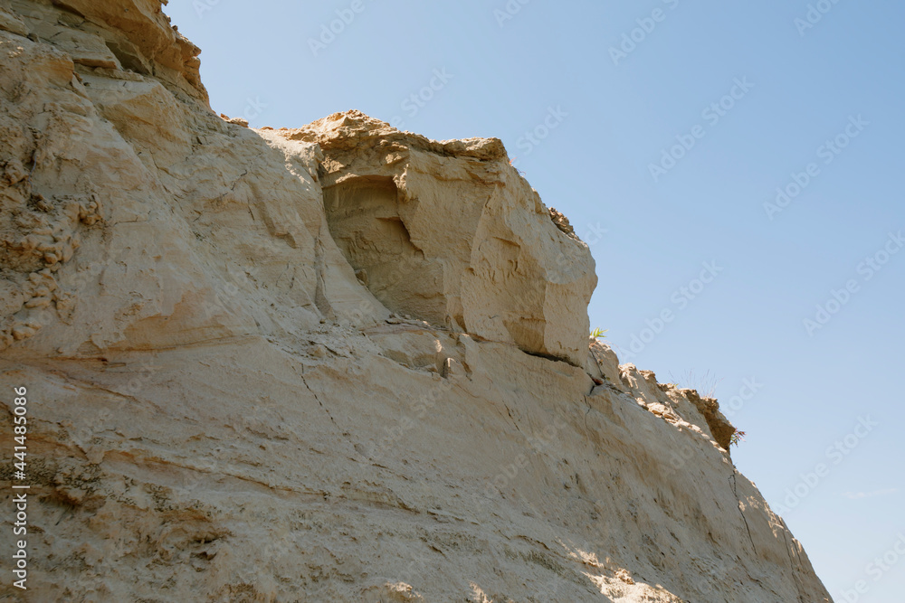 Sandy cliff against the background of a blue clear sky. Sunny day.