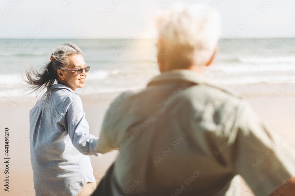 Retired couple holding hand happily walked down to the sandy beach.An elderly wife holding her husband's hand and smile happily. Plan life insurance and retirement concept.	