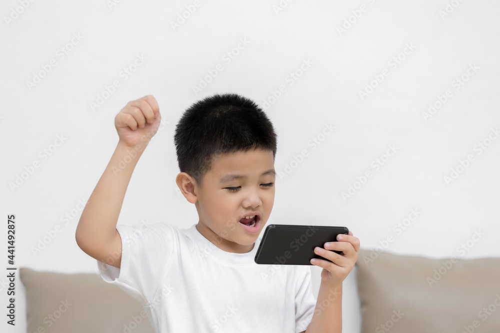 Happy little boy having fun playing game on mobile phone, Preschool kid sitting on sofa with smiling face watching cartoon on smartphone, Child using cell phone while relaxing at home Happy little boy having fun playing game on mobile phone, Preschool kid sitting on sofa with smiling face watching cartoon on smartphone, Child using cell phone while relaxing at home