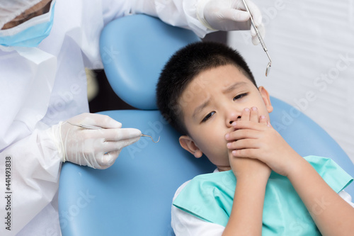 Dentist examining Asian little boy teeth in clinic. Calm and happy
