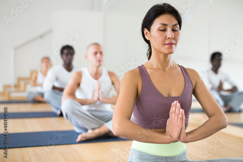 Young woman maintaining healthy lifestyle practicing meditation at group yoga class