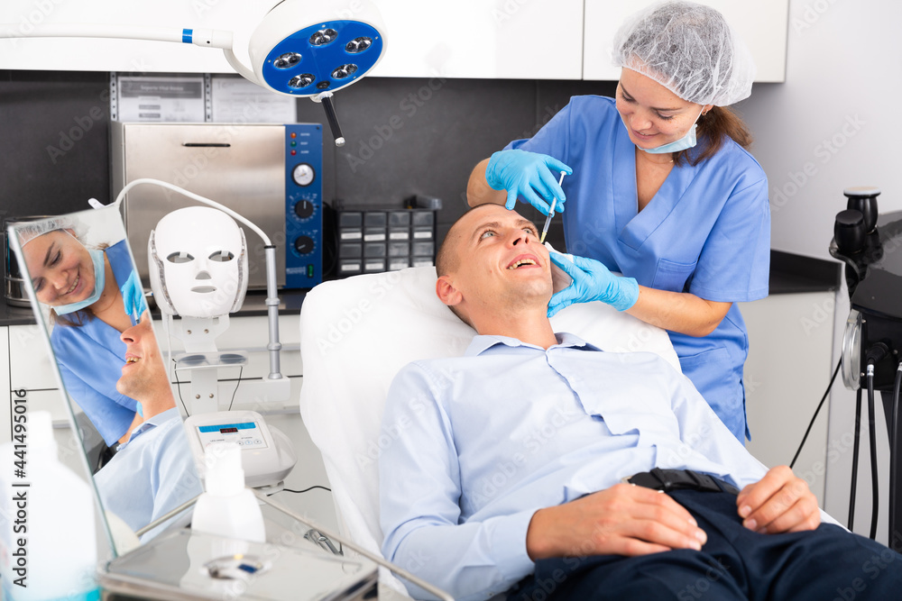 Obraz premium Skilled woman beautician filling males wrinkles using rejuvenating injections in clinic of aesthetic medicine