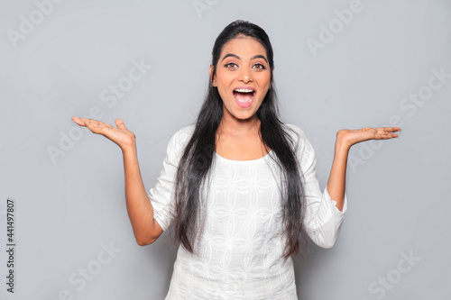 Asian beautiful young pretty woman wearing white Kurti dress feeling extremely happy showing her both hand posing isolated over gray background photo