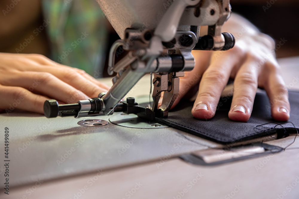Close up craftsman hands sew stuff blank for wallet use sewing machine. Working at leather workshop Close up craftsman hands sew stuff blank for wallet use sewing machine. Working at leather workshop