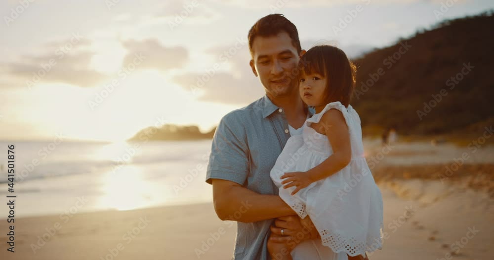 Attractive young dad holding his daughter at the beach at sunset, making precious memories together Attractive young dad holding his daughter at the beach at sunset, making precious memories together