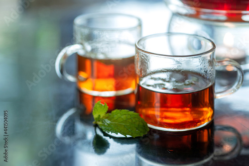 Hot black tea with fresh mint leaves, transparent cup of tea and teapot, closeup photo