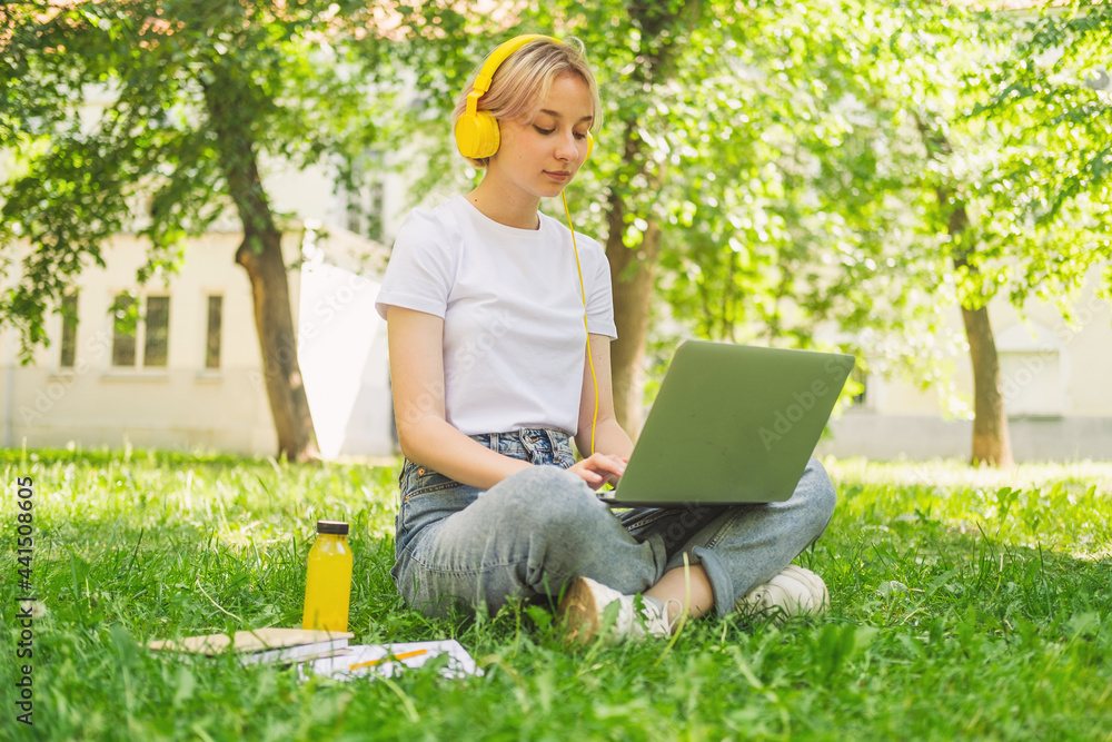 Cute girl is sitting in the park in headphones with a laptop Cute girl is sitting in the park in headphones with a laptop