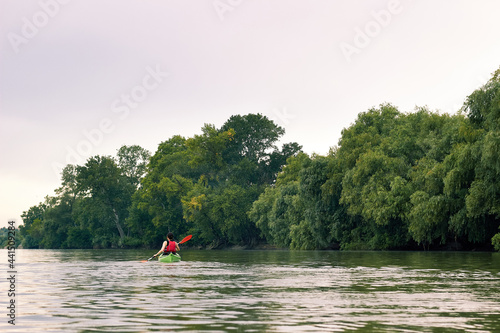 Caucasian young woman tourist paddling the green kayak at Danube river at summer near trees. Kayaking, travel, leisure concept.
