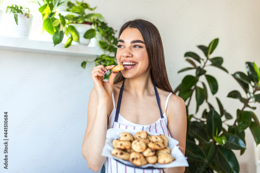Young beautiful housewife holding freshly baked cookies on a tray in the kitchen.