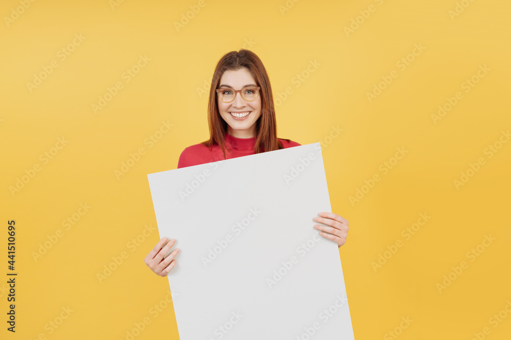 Happy vivacious young woman holding a blank white sign Happy vivacious young woman holding a blank white sign