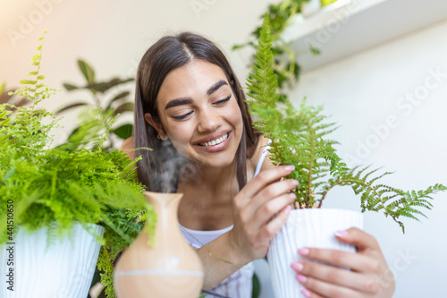 Fényképezés Woman caring for plants next to steam aroma oil diffuser on the table at home, steam from humidifier