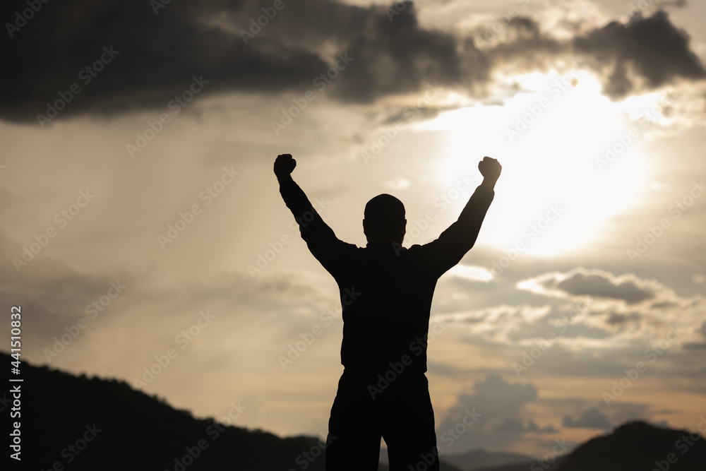 Silhouette Young man raised hand in the air with success goal on sunset background. Man standing on top of the mountain freedom life concept. Silhouette Young man raised hand in the air with success goal on sunset background. Man standing on top of the mountain freedom life concept.