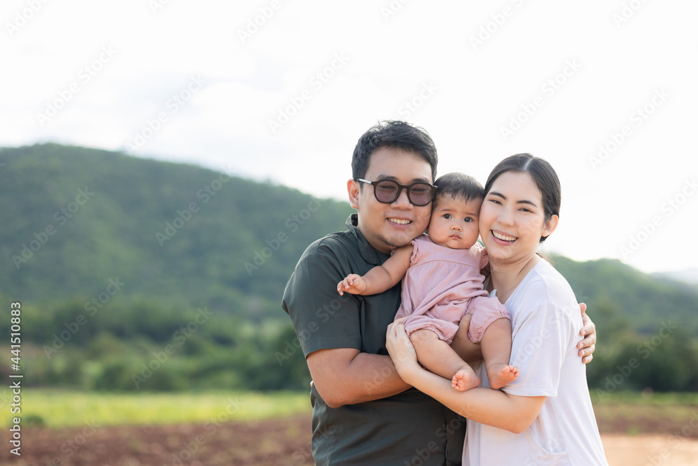Obraz premium Happy asian family father mother child daughter on nature background . Parents hug little baby in arm standing outdoor with sunny day.