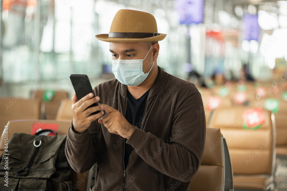 Young traveler man wearing mask protect flu coronavirus. Tourist in airport terminal using smartphone sitting and waiting his flight. During the pandemic must be social distancing self quarantine. Young traveler man wearing mask protect flu coronavirus. Tourist in airport terminal using smartphone sitting and waiting his flight. During the pandemic must be social distancing self quarantine.