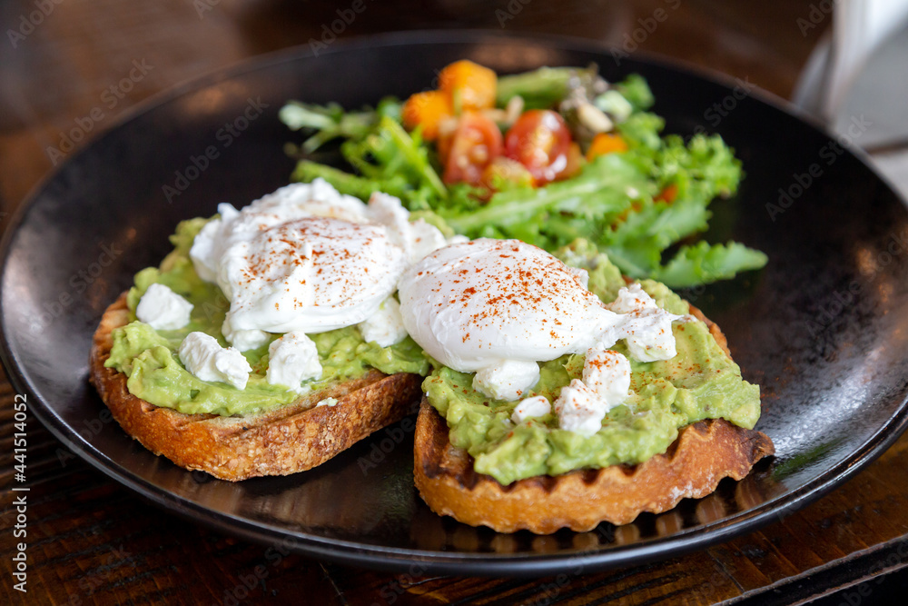 Two avocado toasts with poached eggs and fresh salad on the side, healthy delicious breakfast Two avocado toasts with poached eggs and fresh salad on the side, healthy delicious breakfast