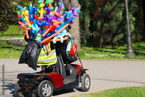 retired riding a scooter with colorful balloons for sale in the park