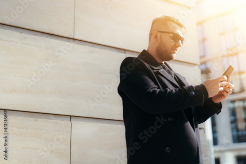  A man with a beard and sunglasses holds a phone in his hands and writes a message near the business center