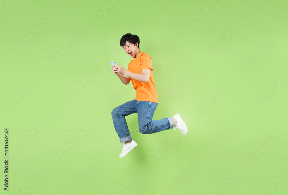 Asian man jumping and holding smartphone , isolated on green Asian man jumping and holding smartphone , isolated on green