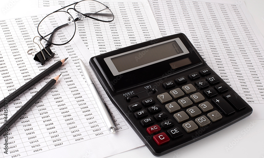 financial charts and graphs on the table with calculator ,pen,pencils and glasses financial charts and graphs on the table with calculator ,pen,pencils and glasses