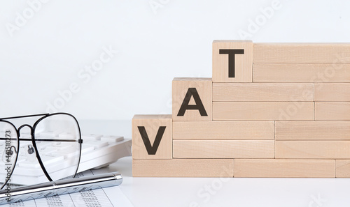 wooden cubes with letters VAT on the white table with keyboard and glasses photo