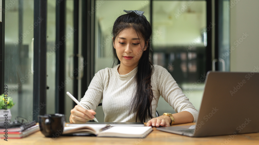 Portrait of female student reading book and doing homework with laptop in study room Portrait of female student reading book and doing homework with laptop in study room