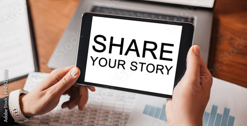 Man hands holding tablet with text Share your story at workplace. Businessman working at desk with documents
