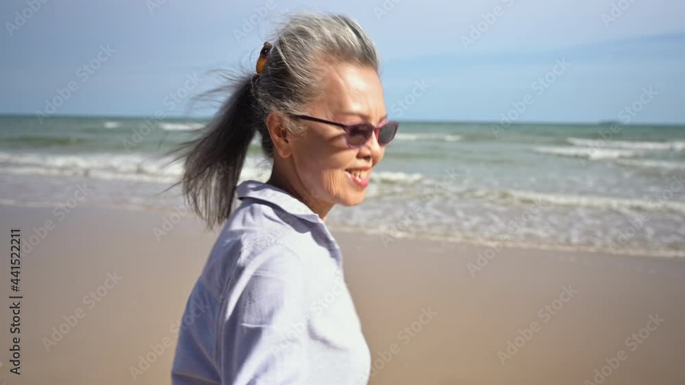 Asian senior woman wearing sunglasses smiling and hand holding husband running from beach to sea in summer holiday. Happy family couple elderly older retirement relax together in seaside on outdoors. Asian senior woman wearing sunglasses smiling and hand holding husband running from beach to sea in summer holiday. Happy family couple elderly older retirement relax together in seaside on outdoors.