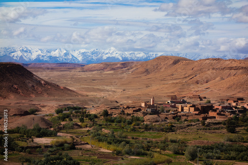 mudbrick village in a green valley with snow on the mountains in the High Atlas mountains with a clear blue sky