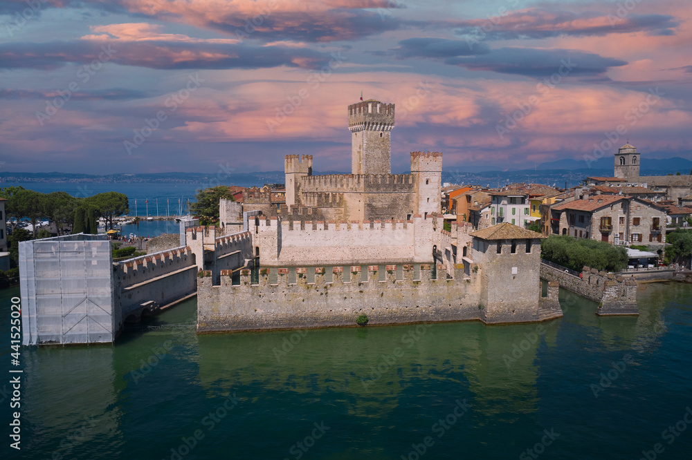 Aerial view of Sirmione castle at sunset, Lake Garda, Italy. Top view of the 13th century castle. Italian castles Scaligero on the water. Pink clouds over Sirmione, Lake Garda in Italy.