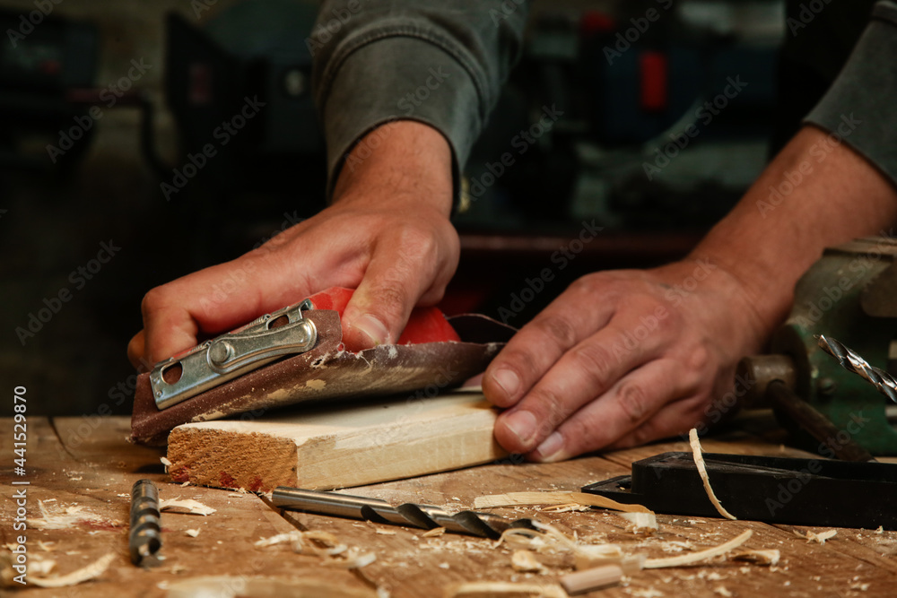 Carpenter is using sandpaper on a piece of wood in workshop. Sanding wooden plank. Carpenter is using sandpaper on a piece of wood in workshop. Sanding wooden plank.