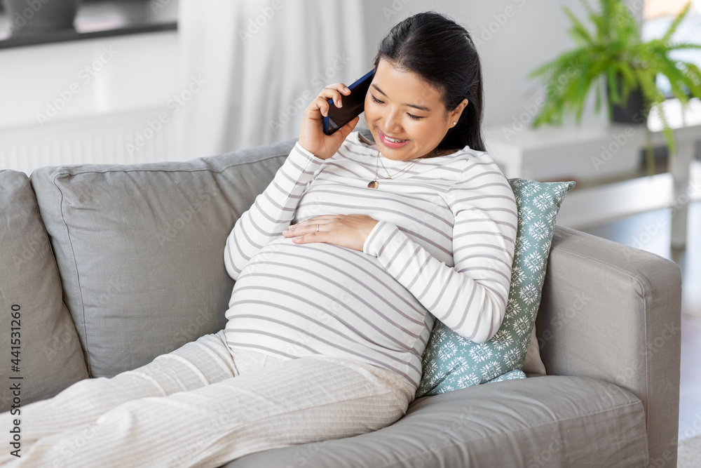 pregnancy, rest, people and expectation concept - happy smiling pregnant asian woman sitting on sofa at home and calling on smartphone pregnancy, rest, people and expectation concept - happy smiling pregnant asian woman sitting on sofa at home and calling on smartphone