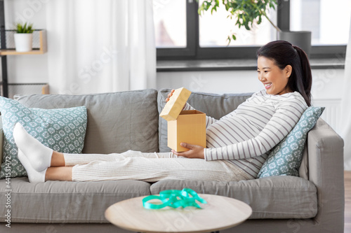 pregnancy, holidays and people concept - happy smiling pregnant asian woman opening gift box sitting on sofa at home