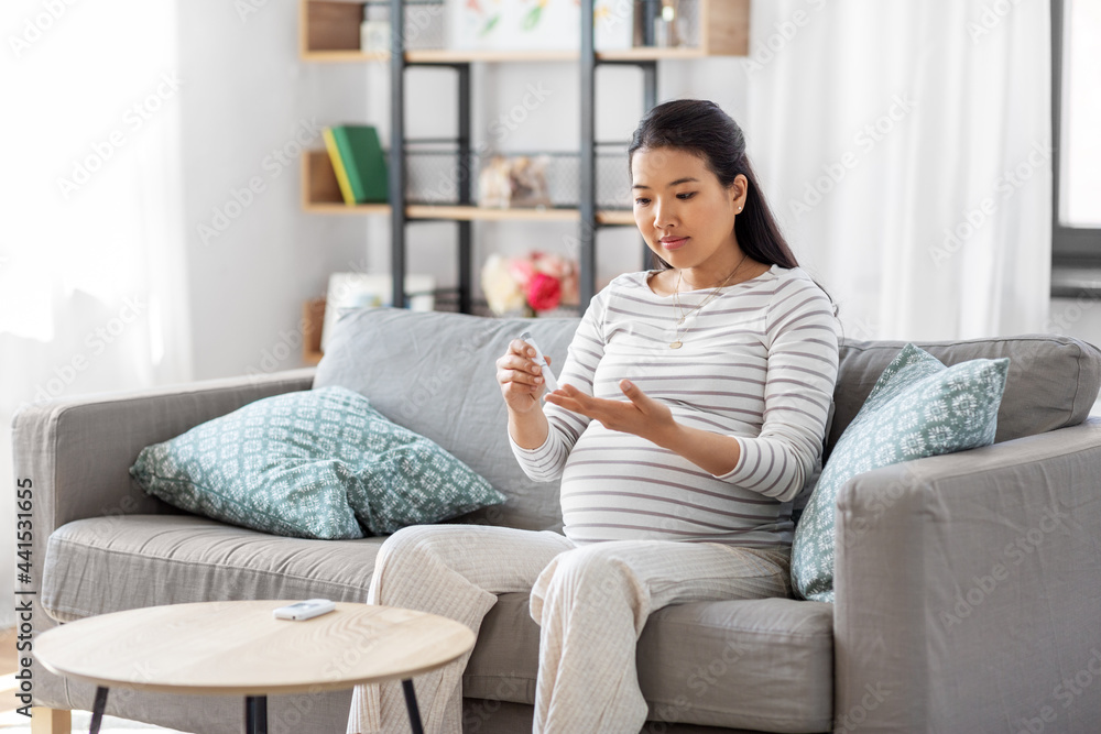 pregnancy, health and glycemia concept - pregnant asian woman checking blood sugar level with glucometer and lancing device at home pregnancy, health and glycemia concept - pregnant asian woman checking blood sugar level with glucometer and lancing device at home