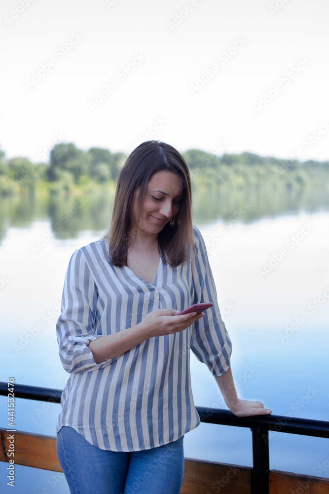 A young freelancer women works outside the office. She uses the phone at the cottage by the river. Forest and river in the background. A business woman works outside the office, Texting A young freelancer women works outside the office. She uses the phone at the cottage by the river. Forest and river in the background. A business woman works outside the office, Texting