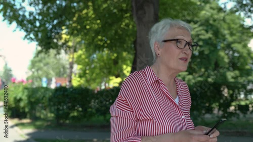 Portrait of senior woman in the park walking while texting.